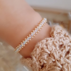 May include: A gold bracelet with iridescent clear beads. The bracelet is on a person's wrist.