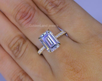 May include: A gold engagement ring with a large emerald cut diamond and a pave diamond band. The ring is on a person's finger.