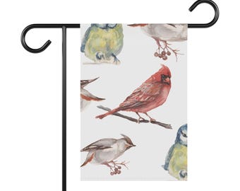 May include: A garden flag featuring watercolor illustrations of various birds, including a vibrant red cardinal perched on a branch. The flag has a white background and is displayed on a black metal stand.