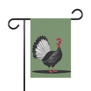 May include: A garden flag with a stylized illustration of a turkey. The turkey has black and white feathers, a red head and wattle, and red feet. The flag is mounted on a black metal stand, with a green background.