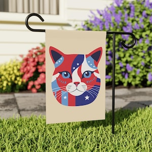 May include: A cream-colored garden flag with a red, white, and blue cat face design. The cat's eyes are blue, and the design features stars and stripes.