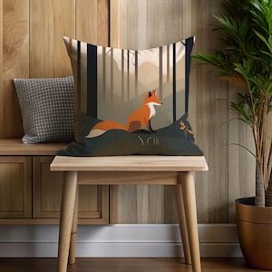 May include: A decorative throw pillow with a forest scene featuring a fox sitting in the middle of the image. The pillow is on a wooden bench with a wooden table in front of it. A potted plant is on the right side of the image.
