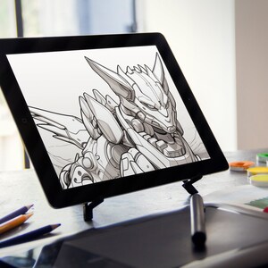 Może przedstawiać: Na tablecie cyfrowym wyświetlony jest czarno-biały rysunek robota z głową przypominającą wilka. Tablet leży na biurku ze stylusem, oł&oacute;wkami i zestawem farb akwarelowych.