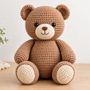 Op de afbeelding: Een gehaakte bruine teddybeer met een crèmekleurige snuit en bijpassende crèmekleurige ronde patches op de voetzolen. De beer heeft twee zwarte plastic ogen, een donkerbruin geborduurde neus en een eenvoudig geborduurde mond.