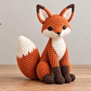 Könnte beinhalten: Ein gehäkelter Fuchs mit einem leuchtend orangefarbenen Körper, einer weißen Brust und Gesichtszeichnung, dunkelbraunen Pfoten und spitzen Ohren mit dunkelbraunen Spitzen. Der Fuchs hat schwarze Sicherheitsaugen und eine kleine schwarze Nase.