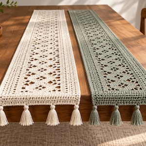 May include: Two rectangular table runners, one in cream and one in sage green, featuring an intricate crocheted geometric pattern with openwork diamond shapes. Each runner is finished with four matching tassels attached to the bottom edge.