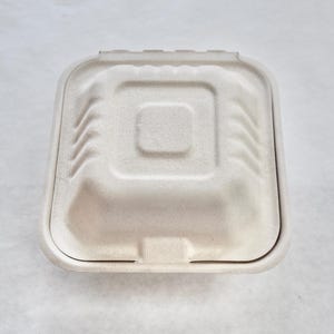 May include: A white cardboard food container with a hinged lid. The container is square shaped with rounded corners and a slightly raised centre.