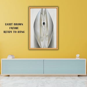 Puede incluir: Impresión de arte abstracto en un marco marrón claro, lista para colgar. La obra presenta un diseño blanco y gris con un centro oscuro. El texto "LIGHT BROWN FRAME READY TO HANG" es visible.