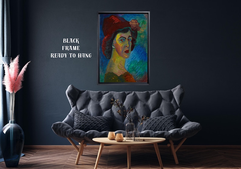 May include: A framed portrait of a woman wearing a red hat with a flower, set against a colorful background. The artwork is displayed above a gray sofa with black pillows. The text "BLACK FRAME READY TO HANG" is visible.