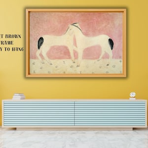 以下が含まれることがあります： ピンクとベージュの背景に、黒い模様のある2頭の白い馬が描かれた額入りのアートワーク。アートワークは薄茶色のフレームに入っており、すぐに飾ることができます。「LIGHT BROWN FRAME READY TO HANG」というテキストが表示されています。