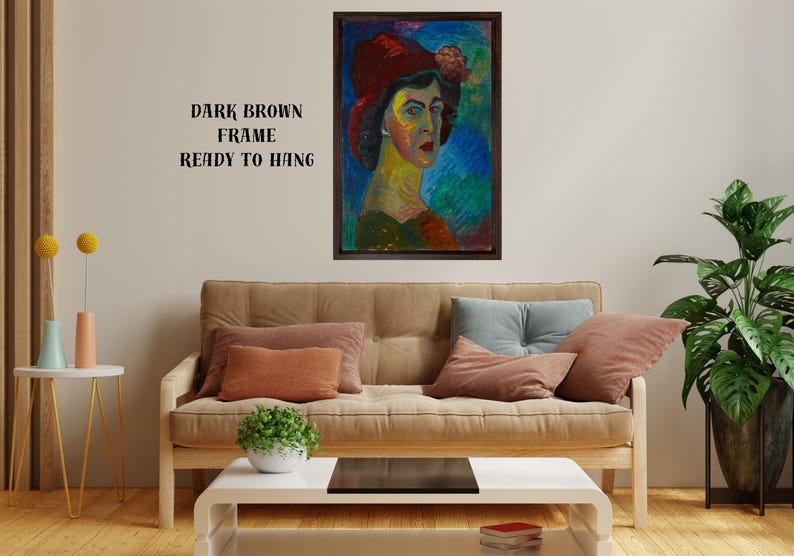 May include: A framed portrait of a woman wearing a red hat, with a dark brown frame. The painting features vibrant colors and brushstrokes. Text on the wall reads "DARK BROWN FRAME READY TO HANG". The artwork is displayed above a sofa with pillows.