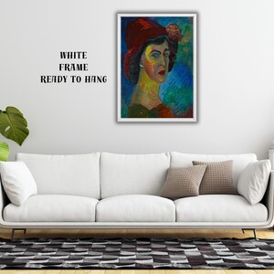 May include: A framed portrait of a woman wearing a red hat with a flower, painted in vibrant colors. The artwork is displayed above a white sofa, with the text "WHITE FRAME READY TO HANG" visible.