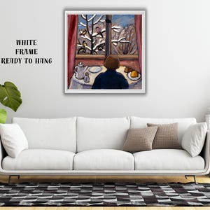 May include: A framed painting depicts a person seated at a table, gazing out a window at a snowy landscape with birds. The artwork features a white frame and the text "WHITE FRAME READY TO HANG". The painting is displayed above a white sofa.