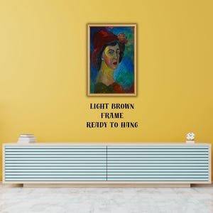 May include: A framed portrait of a woman wearing a red hat, with a light brown frame. The painting features a colorful, impressionistic style. Text below the frame reads "LIGHT BROWN FRAME READY TO HANG".