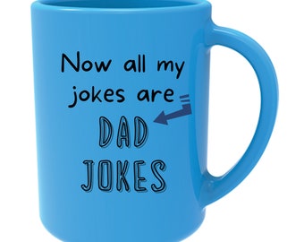 May include: A light blue ceramic mug with a white handle. The mug has black text that reads "Now all my jokes are DAD JOKES" with an arrow pointing to the word "DAD".