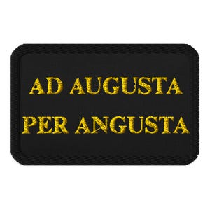 以下が含まれることがあります： 「AD AUGUSTA PER ANGUSTA」と金色の刺繍が施された黒い長方形のパッチ。パッチにはステッチされたボーダーがあります。テキストはセリフ体です。
