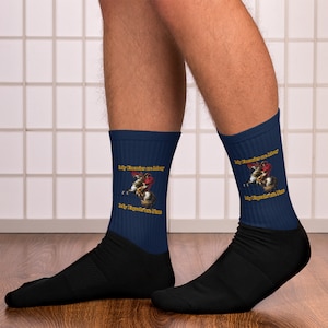 May include: A pair of navy blue socks featuring a graphic of a man on horseback. The socks have the text "My Enemies are Many, My Equals are None" in gold lettering.