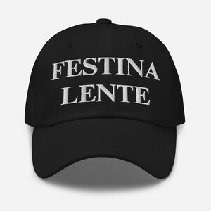 May include: A black baseball cap with white embroidered text that reads "Festina Lente".