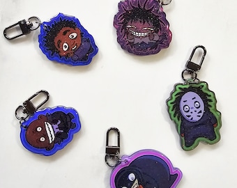 May include: Five cartoon character keychains with black metal clasps. The keychains feature various characters with different colors and designs, including a character with a purple outline and a character with a green outline.