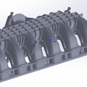 Pode incluir: Um coletor de admissão cinza com múltiplos tubos curvos e uma base retangular. O coletor tem uma superfície texturizada e é projetado para um motor. A imagem é uma renderização 3D.