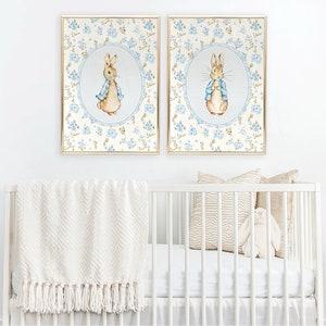 May include: Two framed prints of Peter Rabbit in a blue and white floral pattern. The prints are in gold frames and feature Peter Rabbit wearing a blue jacket.