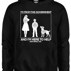 Può includere: Felpa con cappuccio nera con una stampa grafica bianca di una famiglia e un cane. La grafica presenta una silhouette di una donna, un uomo e un cane, tutti con simboli di bersaglio sui loro corpi. Il testo "Sono del governo e sono qui per aiutare. Ruby Ridge, 1992" è stampato sotto la grafica.