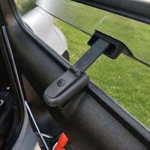 Peut inclure: Un mécanisme de verrouillage de fenêtre de voiture en plastique noir monté sur le panneau de porte intérieur. Le dispositif comprend un bras articulé qui s'étend pour fixer la vitre, avec une vis centrale visible et une finition mate lisse.