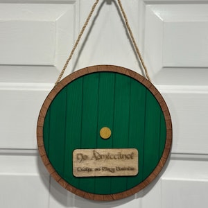 以下が含まれることがあります： 緑色に塗装された丸い木のドアで、茶色の木製のフレームと小さな長方形の看板が付いています。「No Admittance Except on Party Business」と書かれています。吊り下げ用のロープが付いており、直径は約25cmです。