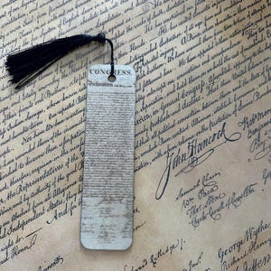 May include: A wooden bookmark featuring the text "Congress Declaration" and a black tassel. The bookmark has a vintage, aged appearance, with a printed design resembling historical documents and signatures.