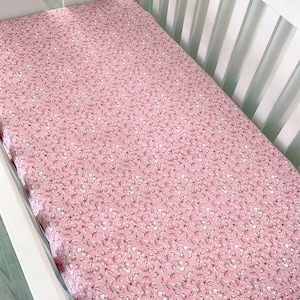 May include: A pink fitted crib sheet with a white floral pattern. The sheet is made of soft, breathable fabric and is perfect for a baby's nursery.