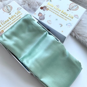 May include: A light green silk baby sleep sack in a white box with a colourful design and the text "Belle Esme Baby Silk" and "DEKO-TEX CERTIFIED TOP GRADE 6A - 22MOMMES MULBERRY SILK THE GIFT OF LOVE FOR YOUR BABY HAIR & SKIN".