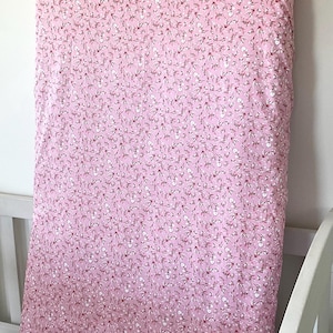 May include: Pink fitted crib sheet with a small white floral pattern.