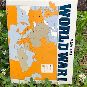 May include: A vintage board game called "World War I" with a map of Europe. The map is divided into territories with numbers and colored in orange, gray, and light blue. The game board is white with blue text.