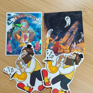 May include: A collection of stickers and a card. The stickers feature a cartoon man playing a saxophone, wearing a yellow vest, black pants, and red shoes. The card has a night sky theme with ghosts and a telescope. One sticker has the word "DEFROSTED".