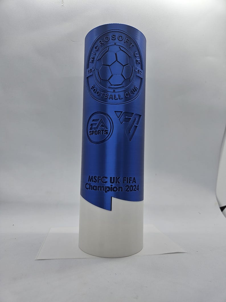May include: A blue trophy with a white base. The trophy has a logo for the Microsoft UK Football Club and the text "MSFC UK FIFA Champion 2024".