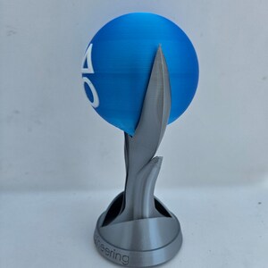 May include: A 3D printed trophy with a blue sphere on top. The sphere has a white logo with the letters "AO" on it. The base of the trophy is gray and has the word "Engineering" inscribed on it.