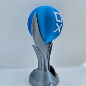 May include: A 3D printed trophy with a blue sphere on top. The sphere has a white logo with the text "Cotten" on it. The base of the trophy is silver and has a stylized design.