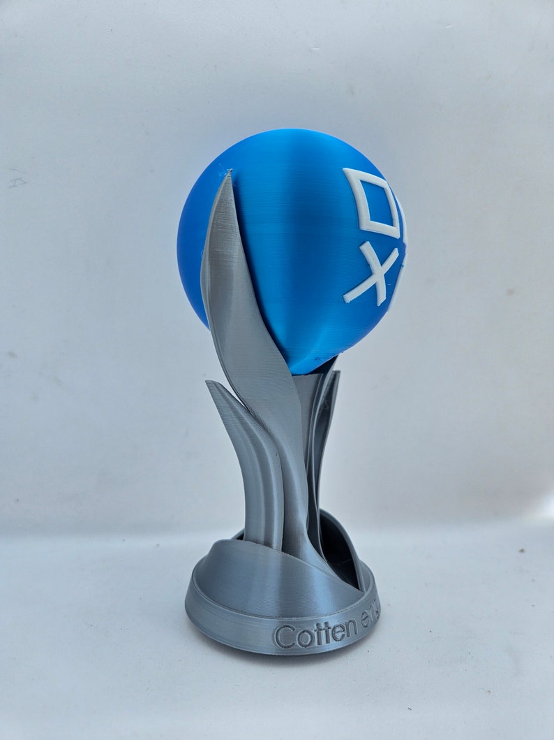 May include: A 3D printed trophy with a blue sphere on top. The sphere has a white logo with the text "Cotten" on it. The base of the trophy is silver and has a stylized design.