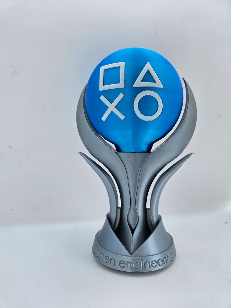 May include: A silver 3D printed trophy with a blue sphere on top. The sphere has the PlayStation button symbols in white. The base of the trophy has the words "otten engineering" inscribed on it.