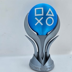 May include: A 3D printed trophy with a blue sphere on top. The sphere has the PlayStation button symbols on it. The base of the trophy is silver and has the words "Cotton Engineering" inscribed on it.