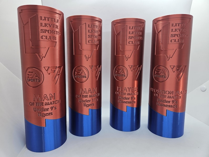 May include: Four red and blue trophy cups with the text "Little Lever Sports Club" and "EA Sports" on them. The trophies are for "Man of the Match" for different age groups.