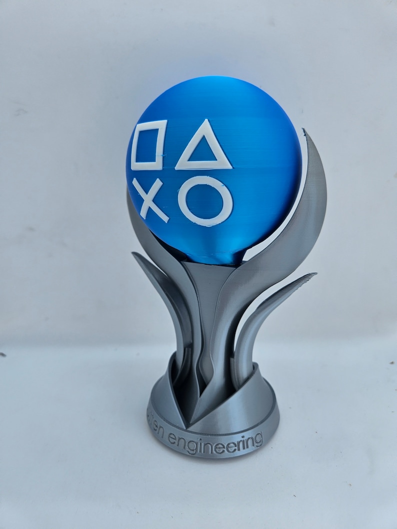 May include: A silver trophy with a blue sphere on top. The sphere has the PlayStation button symbols in white. The base of the trophy says "open engineering".