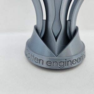 May include: A silver-colored, 3D printed object with a base that reads "often engineering". The object has a unique, geometric design with multiple curved, pointed sections.