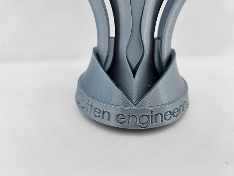 May include: A silver-colored, 3D printed object with a base that reads "often engineering". The object has a unique, geometric design with multiple curved, pointed sections.
