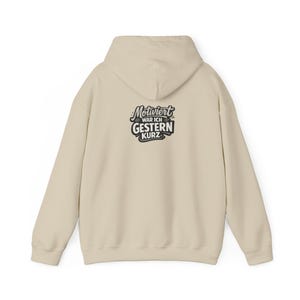 Può includere: Una felpa con cappuccio color beige caratterizzata da una stampa grafica nera sul retro. Il testo "Motiviert war ich gestern kurz" è scritto in un carattere grassetto e stilizzato. Il capo presenta maniche lunghe, un cappuccio, orlo e polsini a coste.