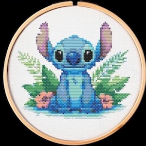 May include: Cross-stitch embroidery of the character Stitch from Lilo & Stitch. The blue alien is surrounded by green foliage and pink flowers. The artwork is framed in a round wooden hoop.