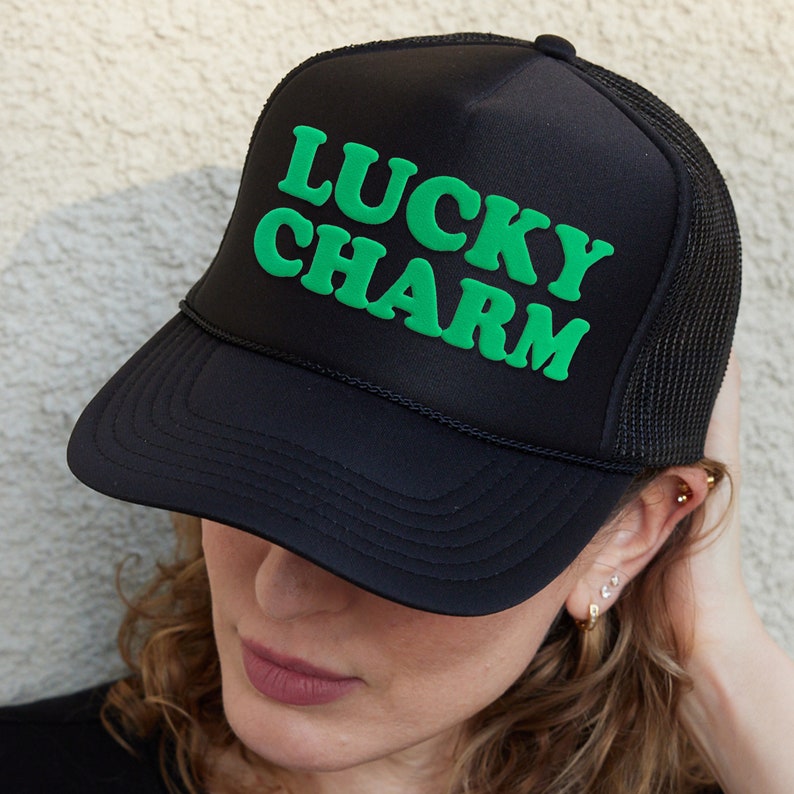 a woman wearing a black trucker hat with the words lucky charm on it