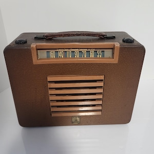 May include: A vintage brown radio with a leather handle and a speaker grill. The radio dial displays numbers from 55 to 160. The radio has a retro design, perfect for collectors or those seeking a nostalgic aesthetic.