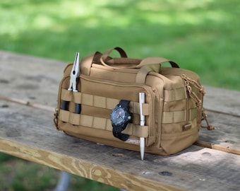 May include: A tan tactical bag with a zipper closure and multiple straps. The bag is filled with a pair of pliers, a pen, and a black wristwatch.