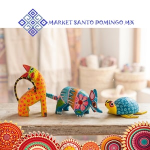 May include: A collection of hand-painted wooden animal ornaments: a giraffe, an armadillo, and a turtle. The giraffe is orange with yellow spots, the armadillo is blue with pink and white details, and the turtle is blue and yellow. The text "MARKET SANTO DOMINGO MX" is visible.